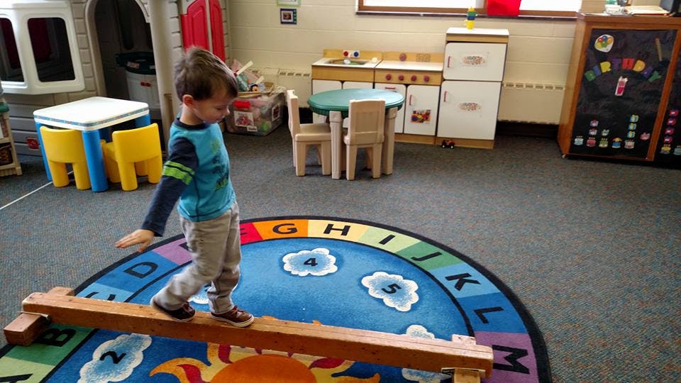 Child walking on a wooden balance beam in a classroom