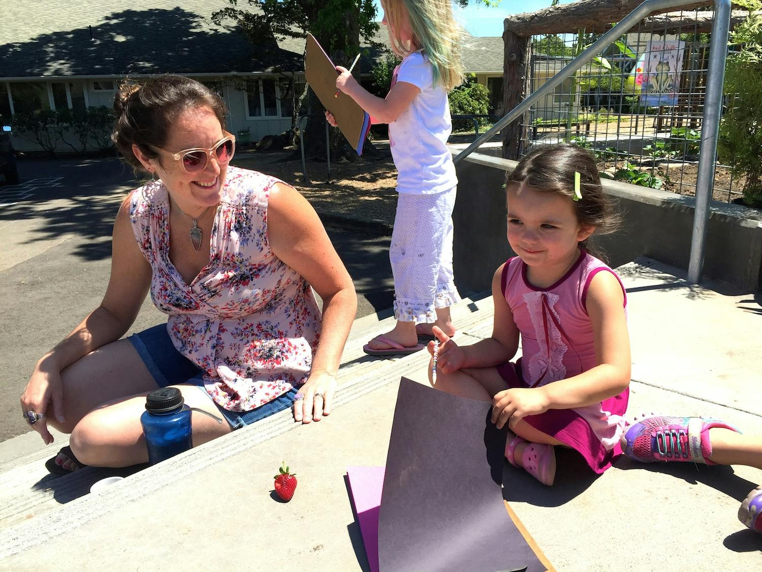 Person and child sitting on steps with paper, another child standing in background