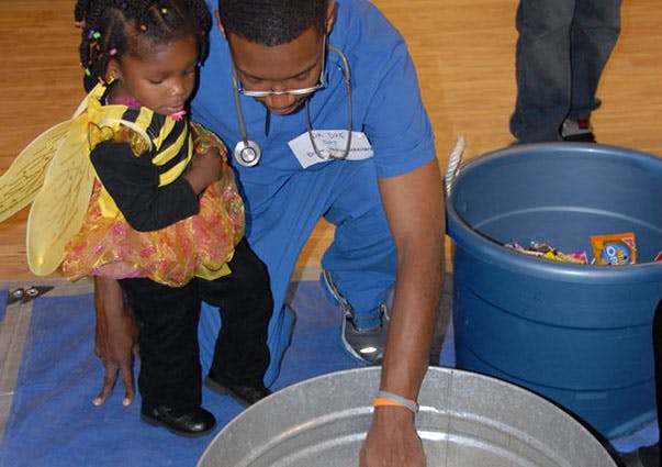 Person in scrubs and child in bee costume looking into a bucket