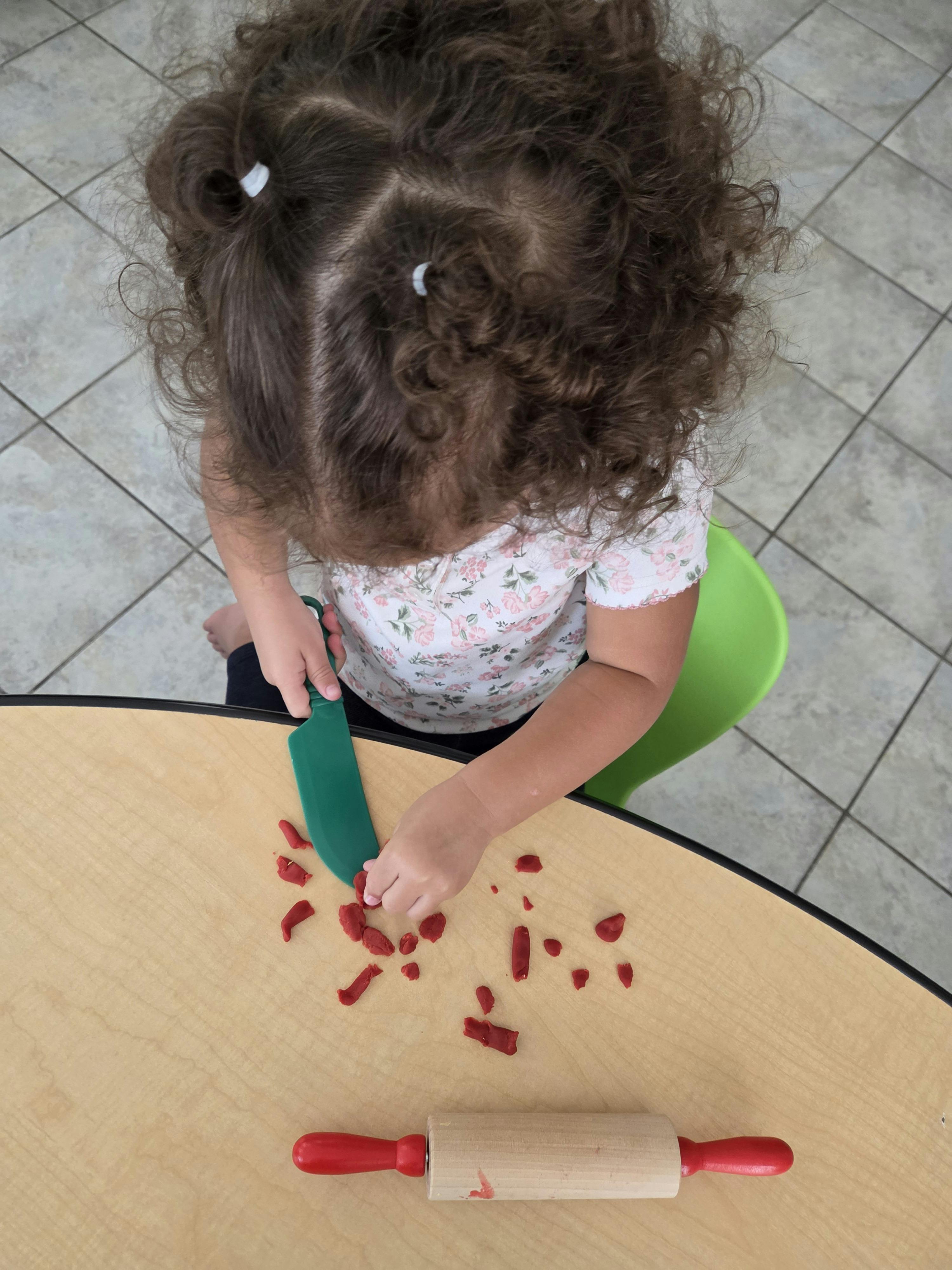 Child cutting red playdough with a plastic toy knife at a table