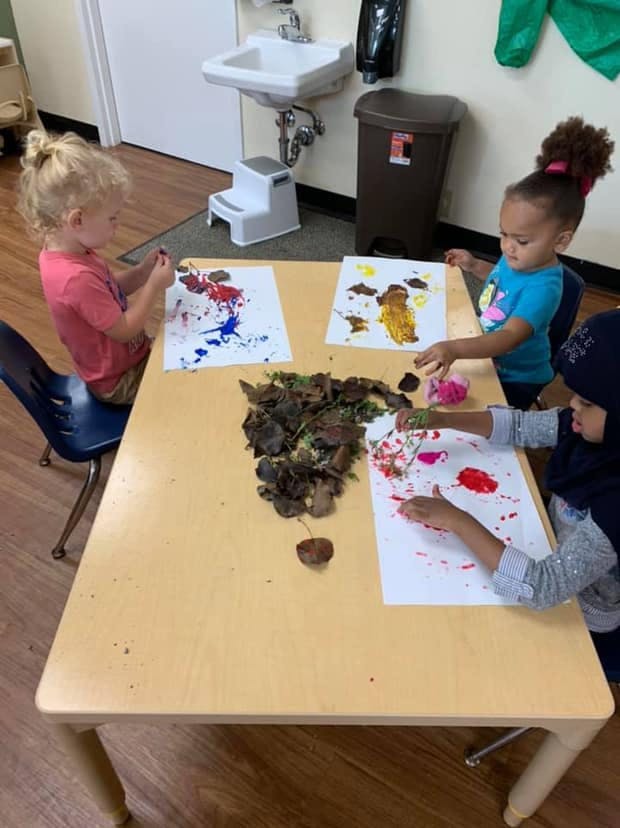 Three children painting at a table in a classroom