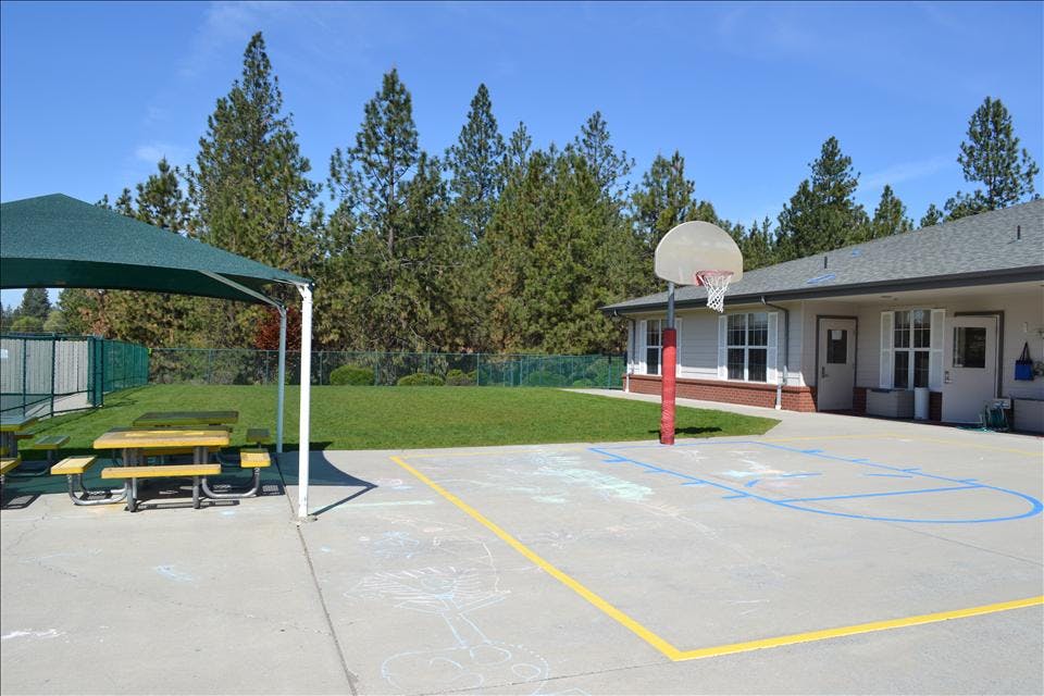 Basketball hoop on court next to building and shaded picnic tables