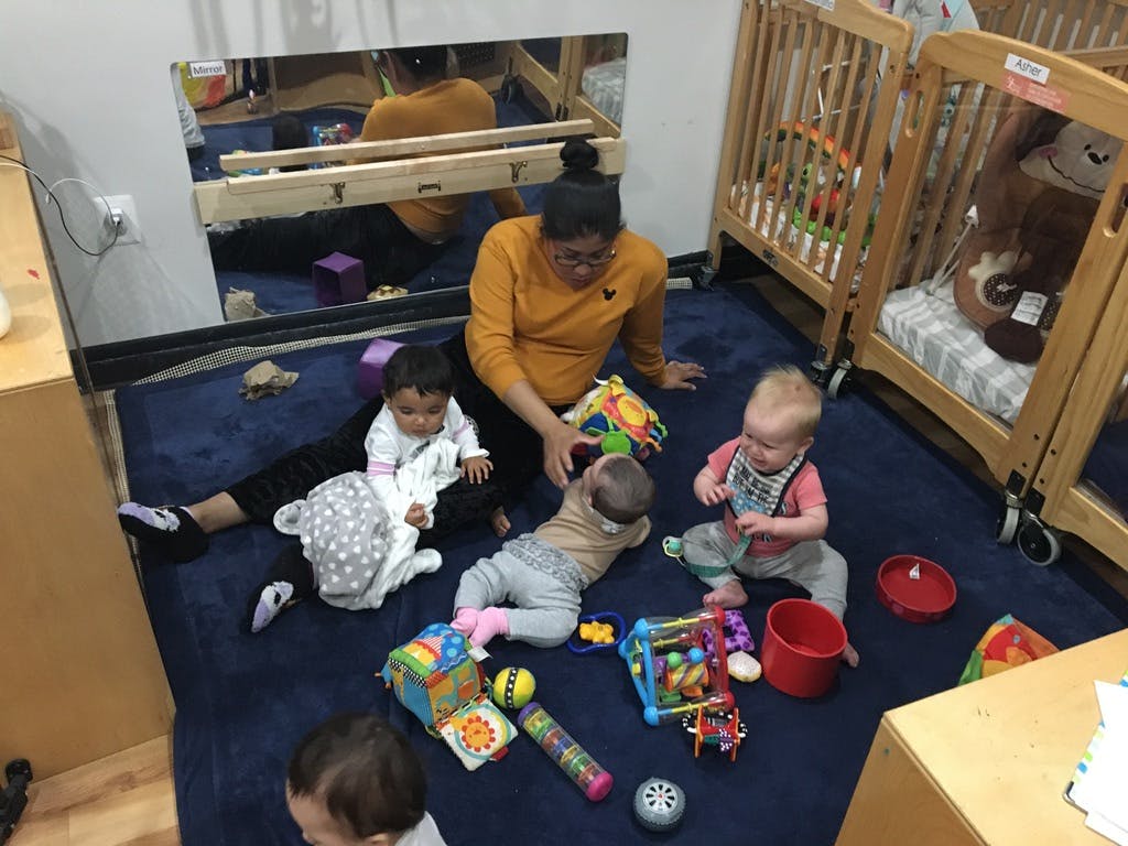 Adult and multiple children playing with toys on a blue rug