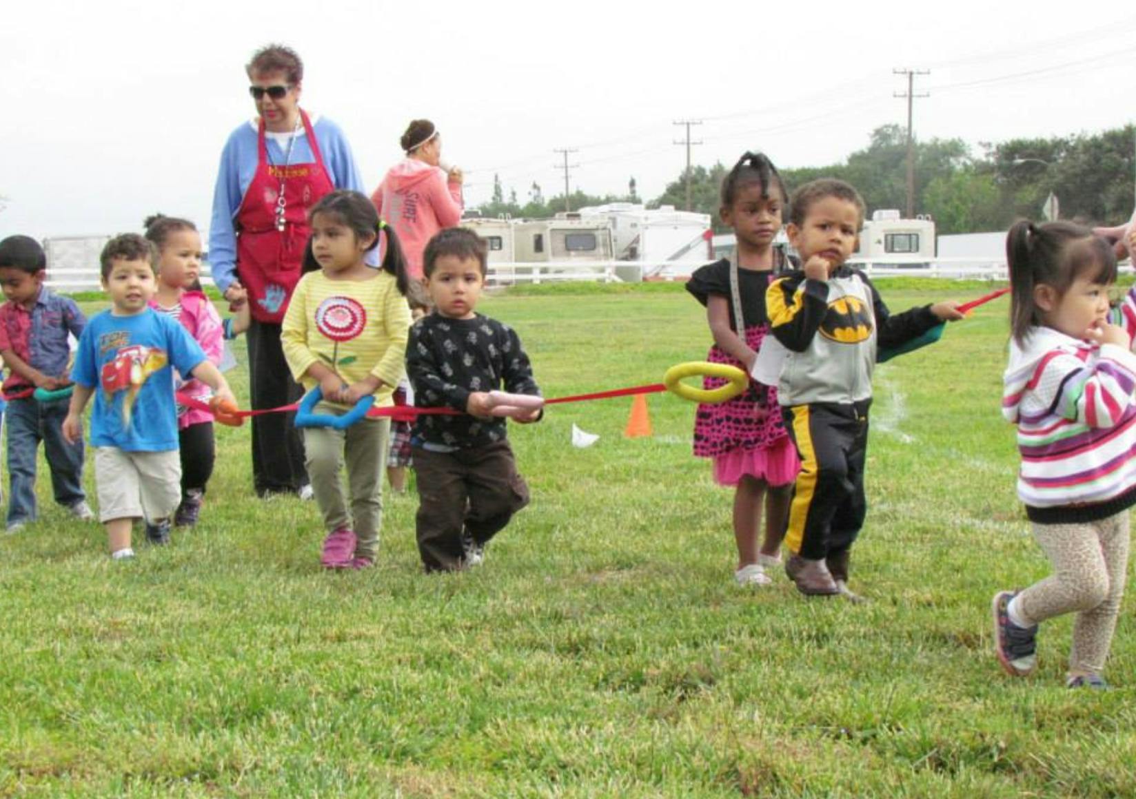 Children playing with a red rope and yellow rings on a grassy field
