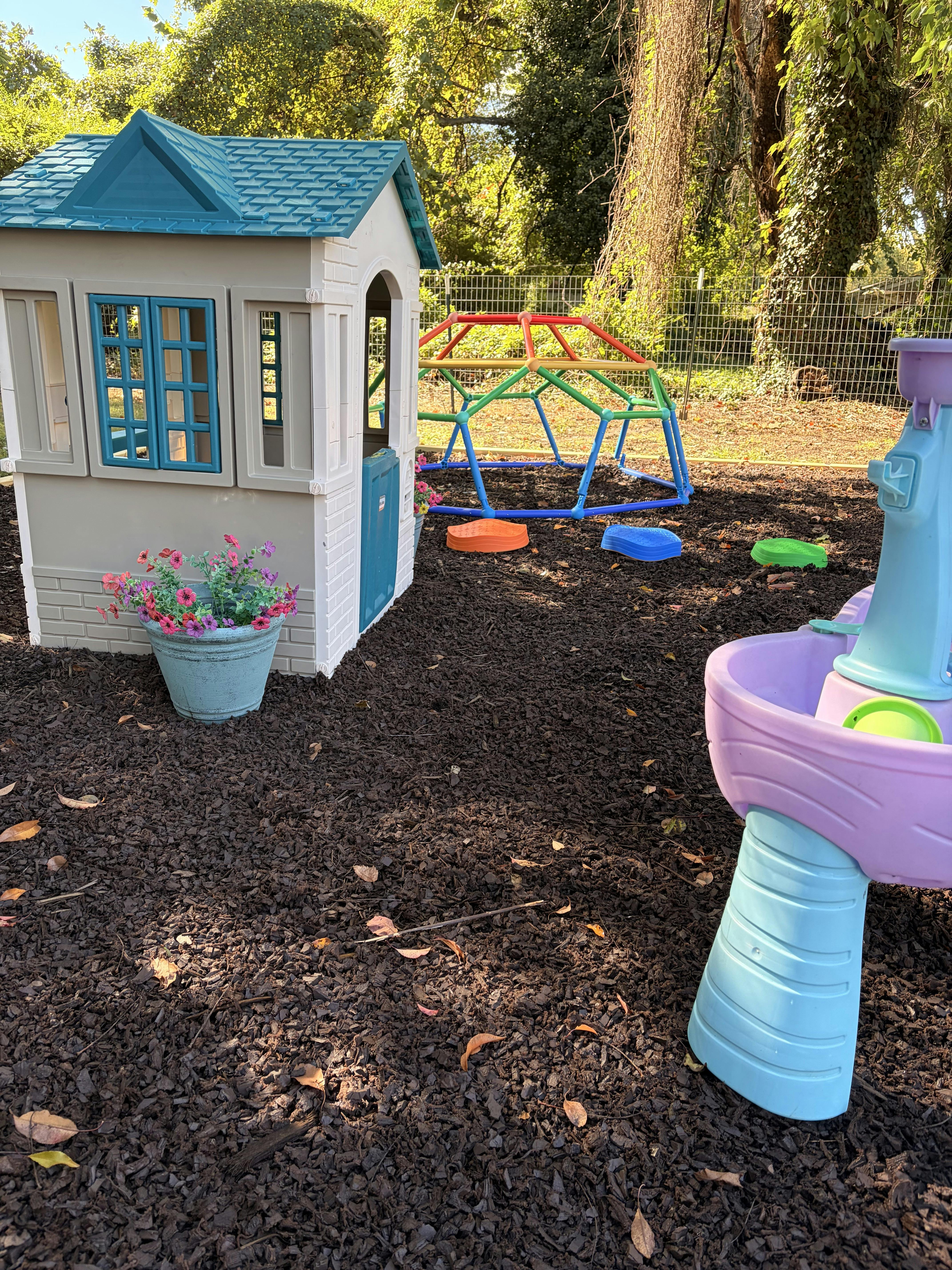 Plastic playhouse, climbing dome, and water table in a backyard