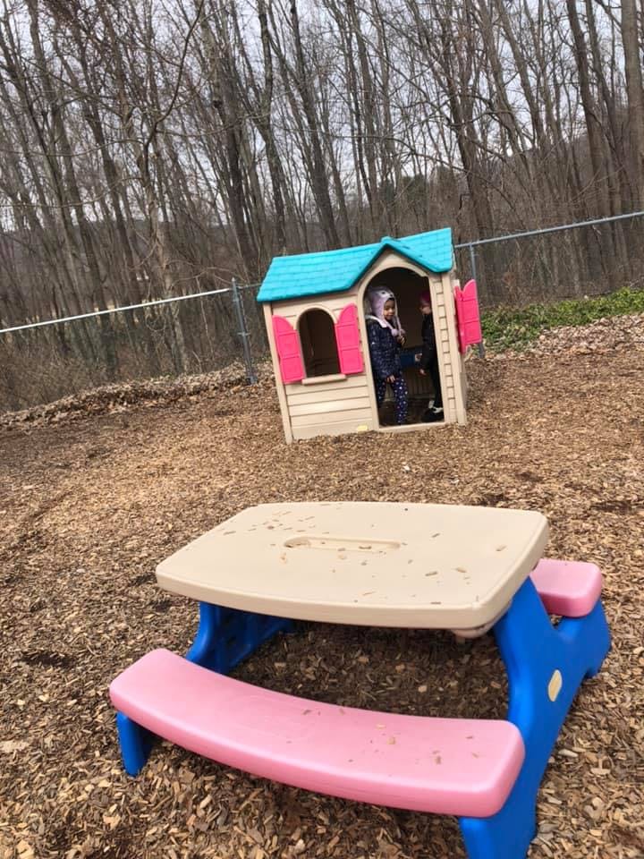 Child in a playhouse with a picnic table in the foreground