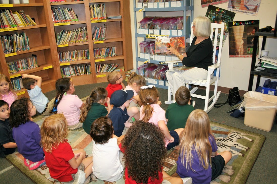 Adult reading a book to a group of children sitting on the floor