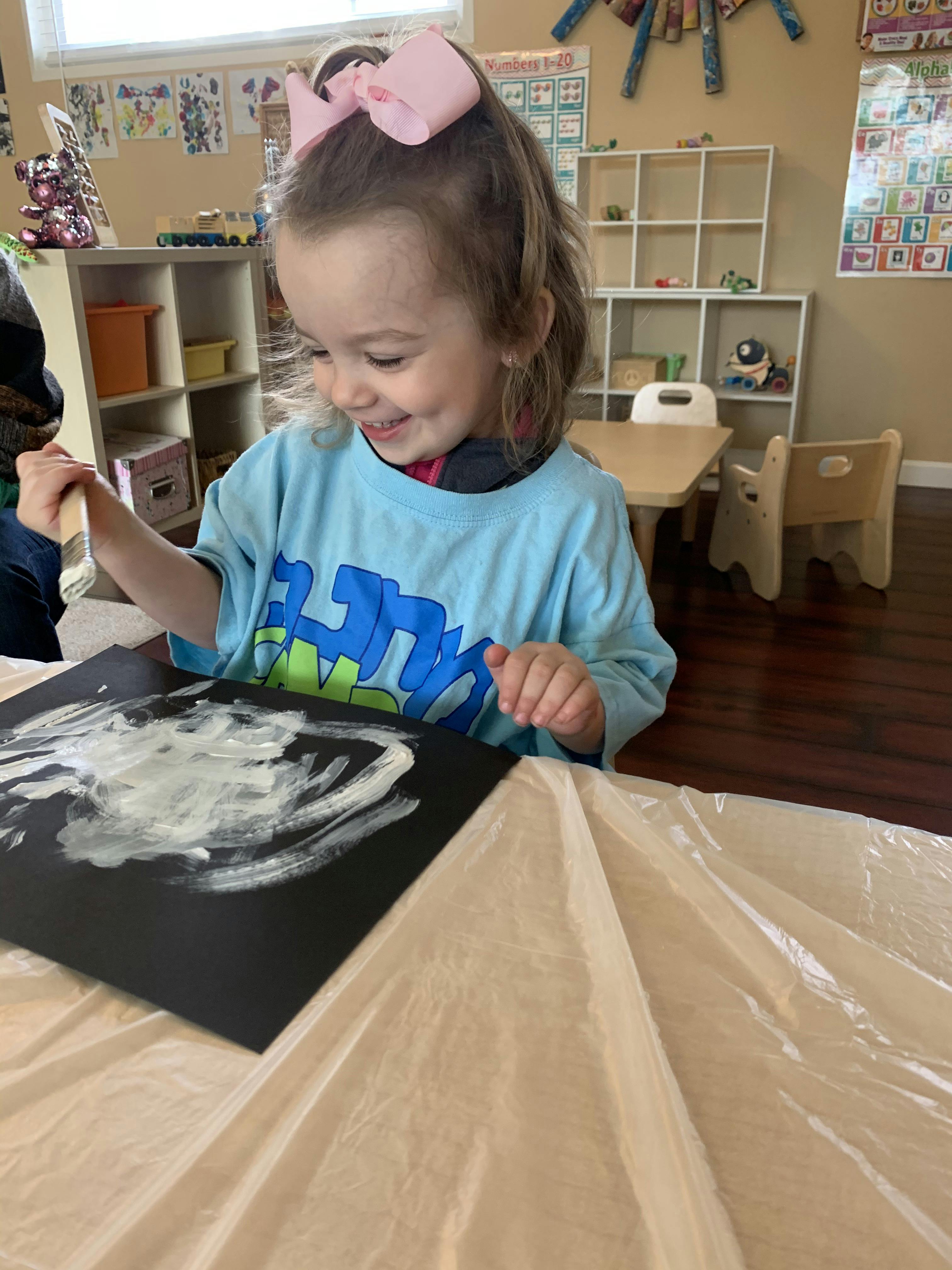 Child painting on black paper with white paint in a classroom
