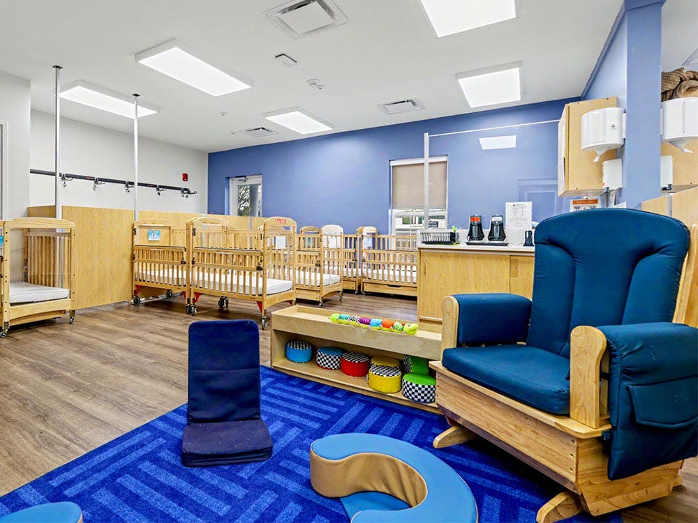 A room with multiple cribs, a blue rug, and a wooden rocking chair