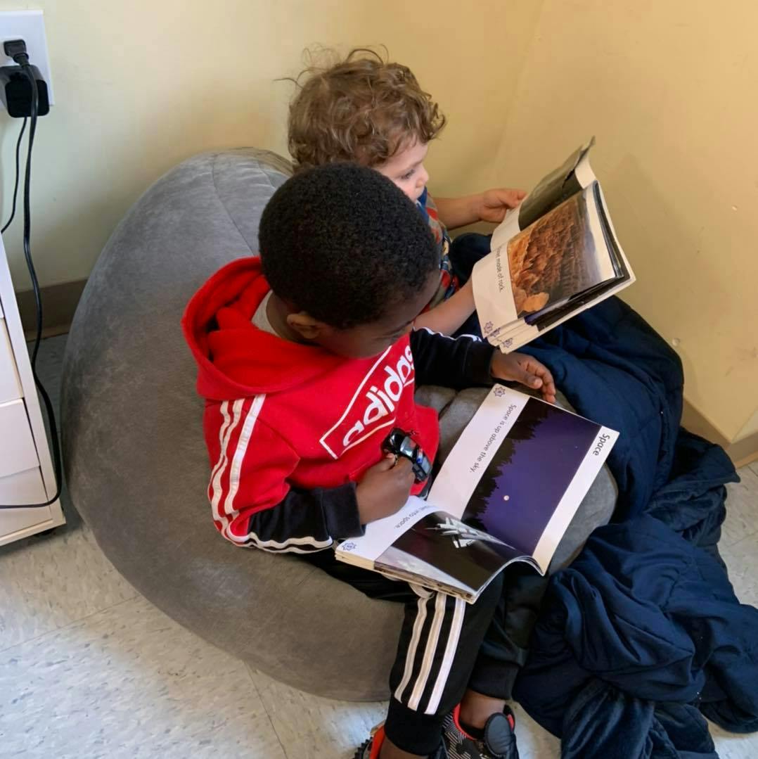 Two children sitting on a beanbag chair reading books