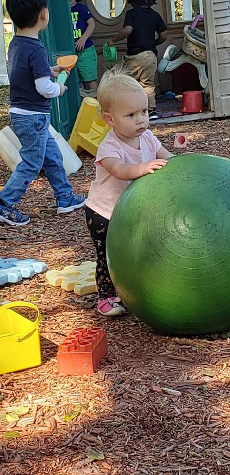 Child standing next to a large green ball on a playground