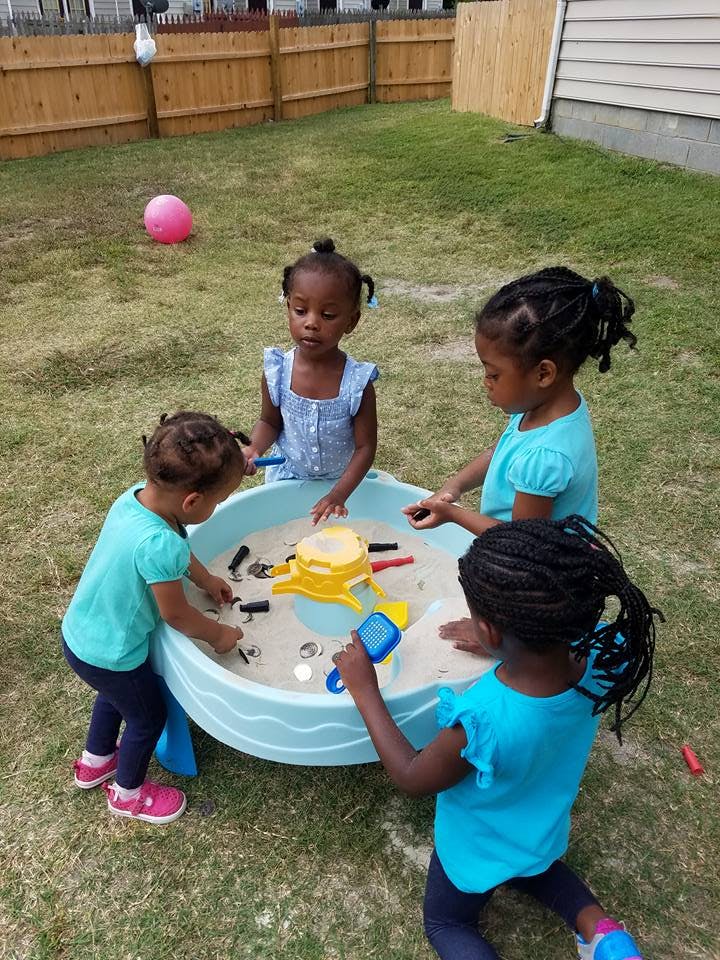 Four children playing around a sand and water table outdoors