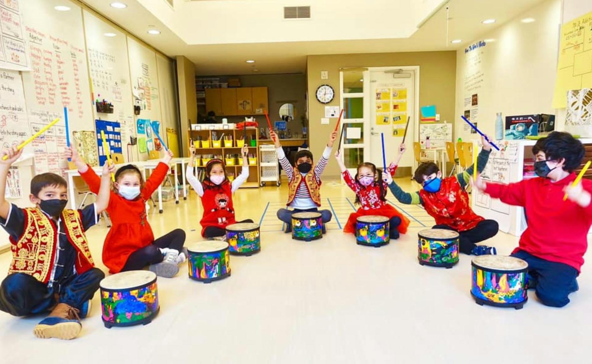 Children in masks playing drums in a classroom