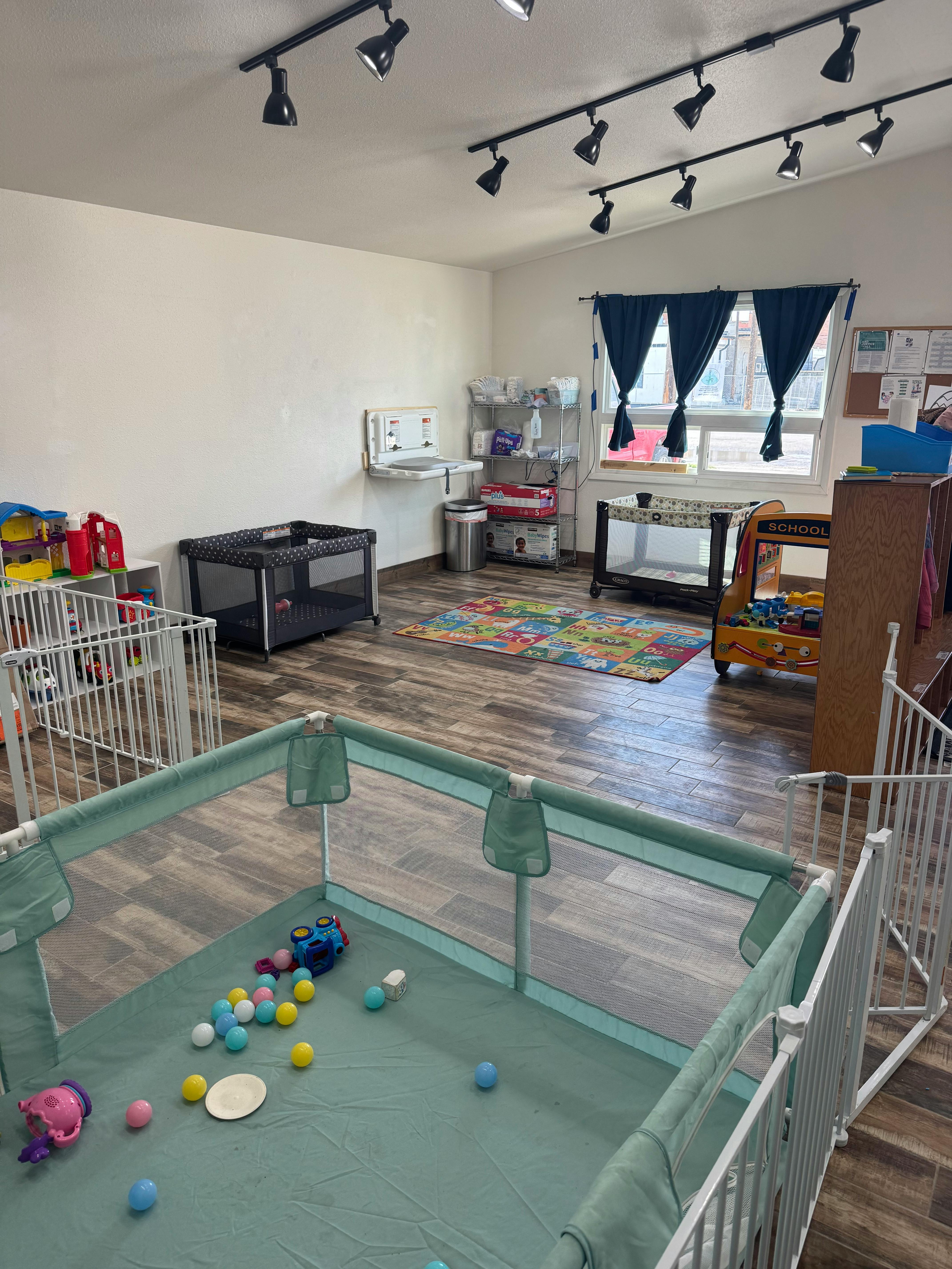 Playpen with colorful balls and toys in a room with cribs and changing station
