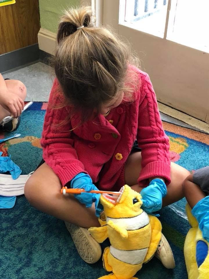 Child in blue gloves brushing teeth of a yellow stuffed animal