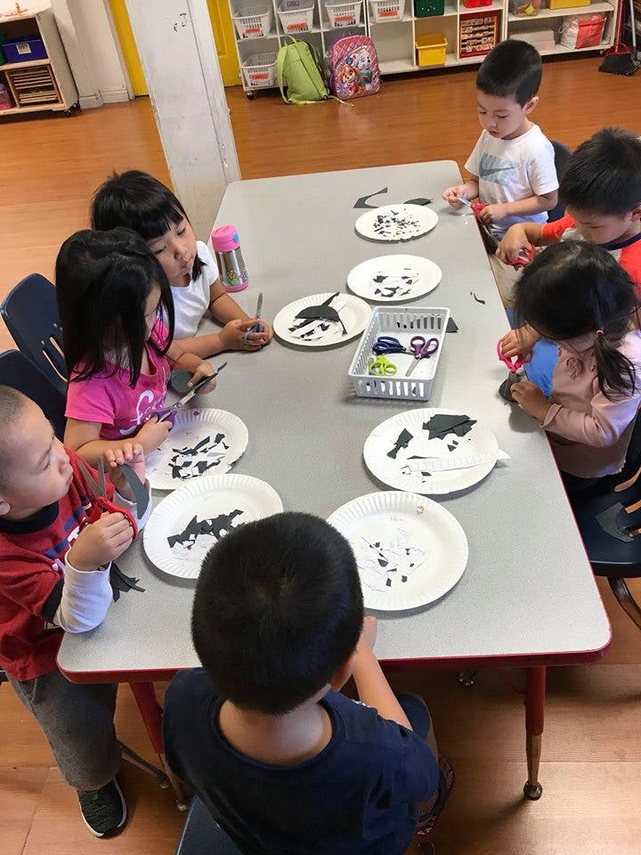 Children sitting at a table doing a craft with paper plates and cutouts