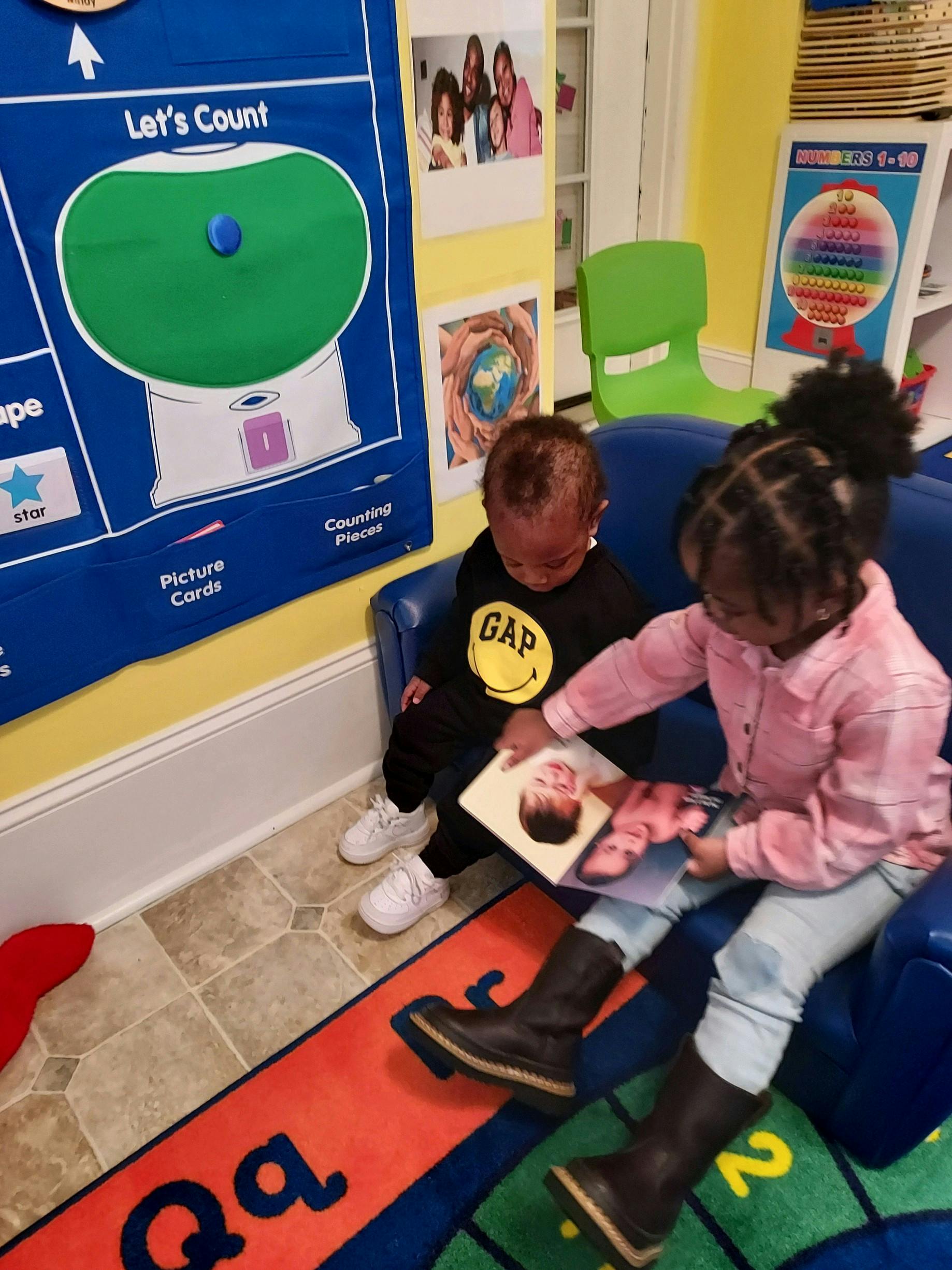 Two children sitting on a blue couch looking at a book together