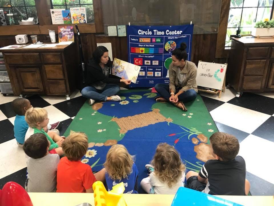 Two people reading a book to a group of children in a classroom