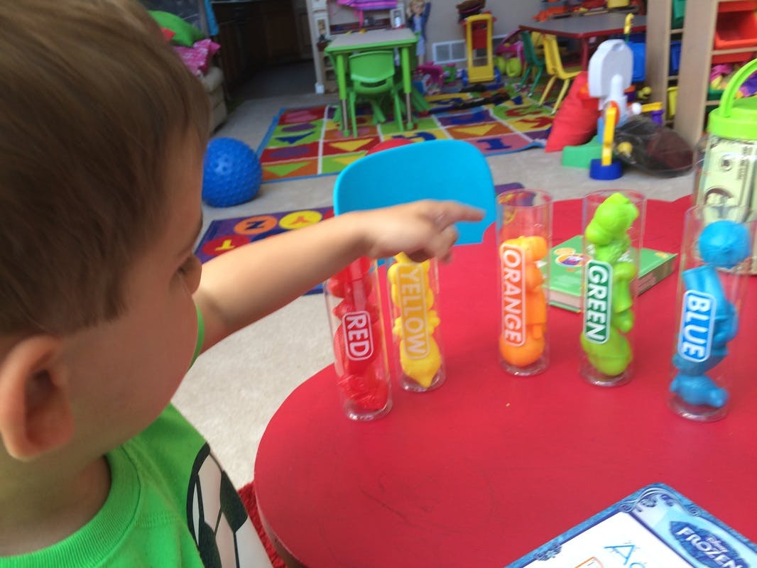 Child pointing at colorful tubes labeled with colors