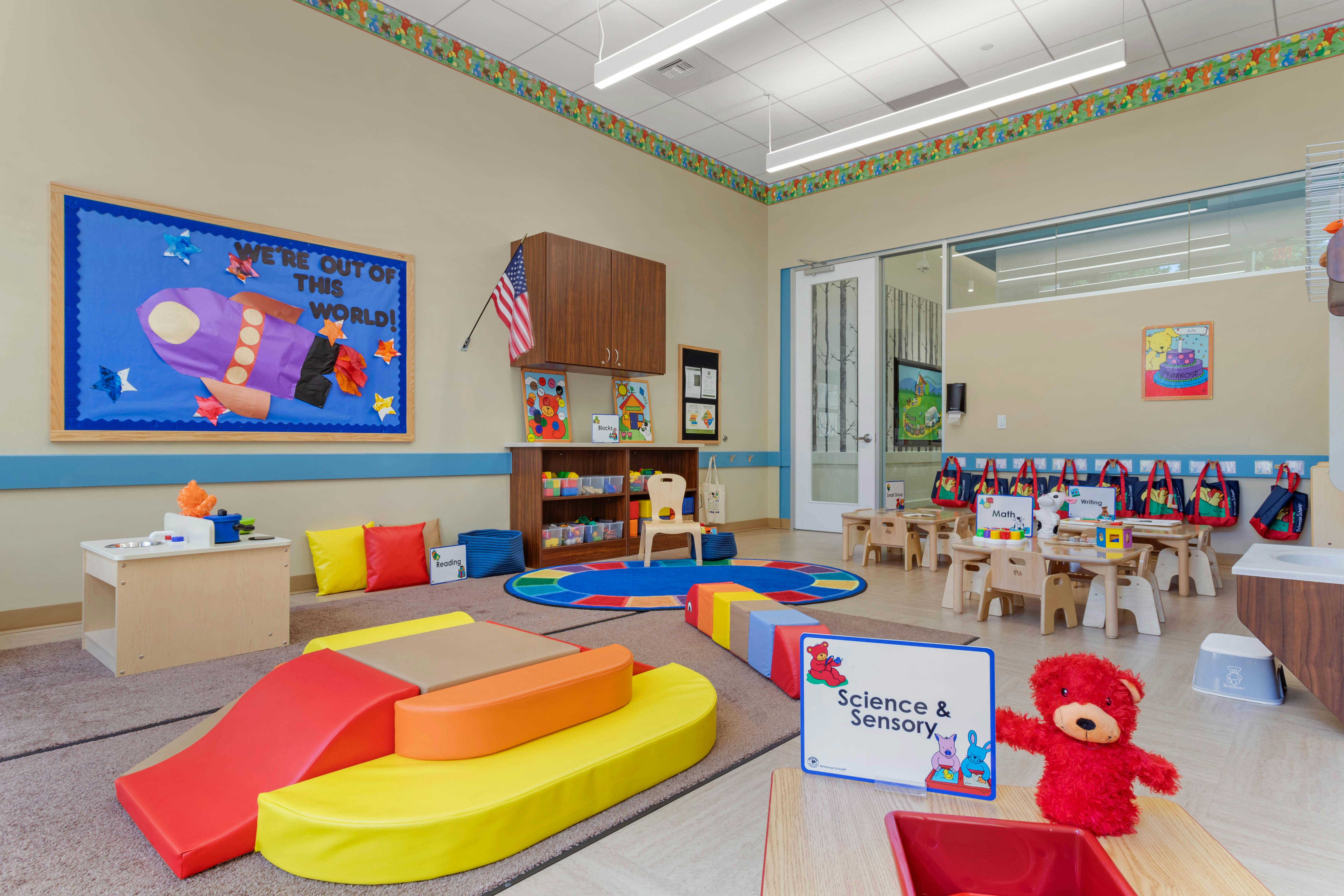 Colorful classroom with play areas, small tables, and a "We're out of this world" bulletin board