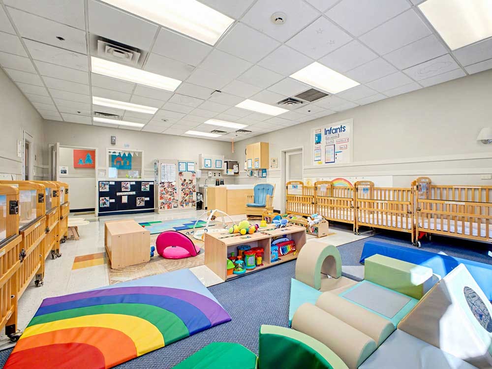 A brightly lit nursery room with multiple cribs, a changing station, and colorful play mats