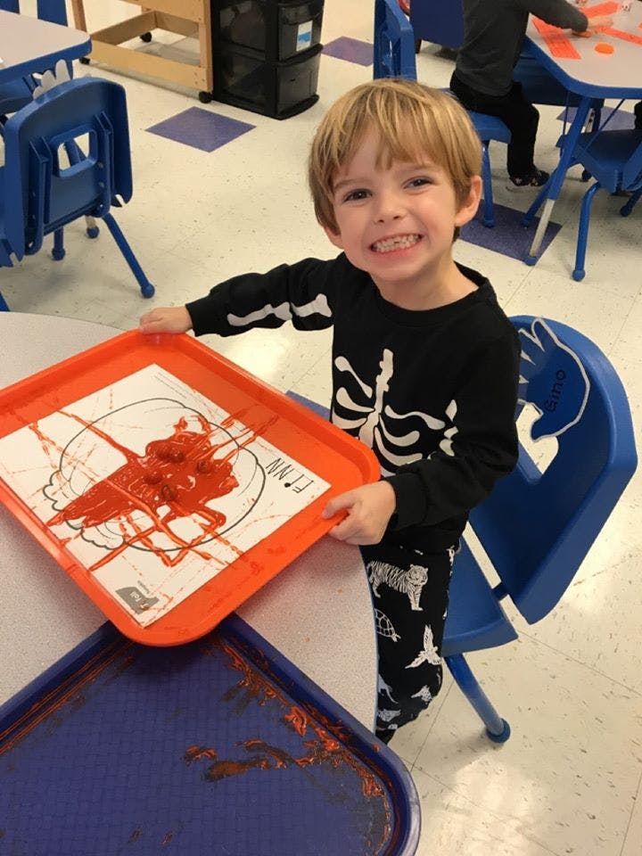 Child holding a tray with red paint on a drawing in a classroom