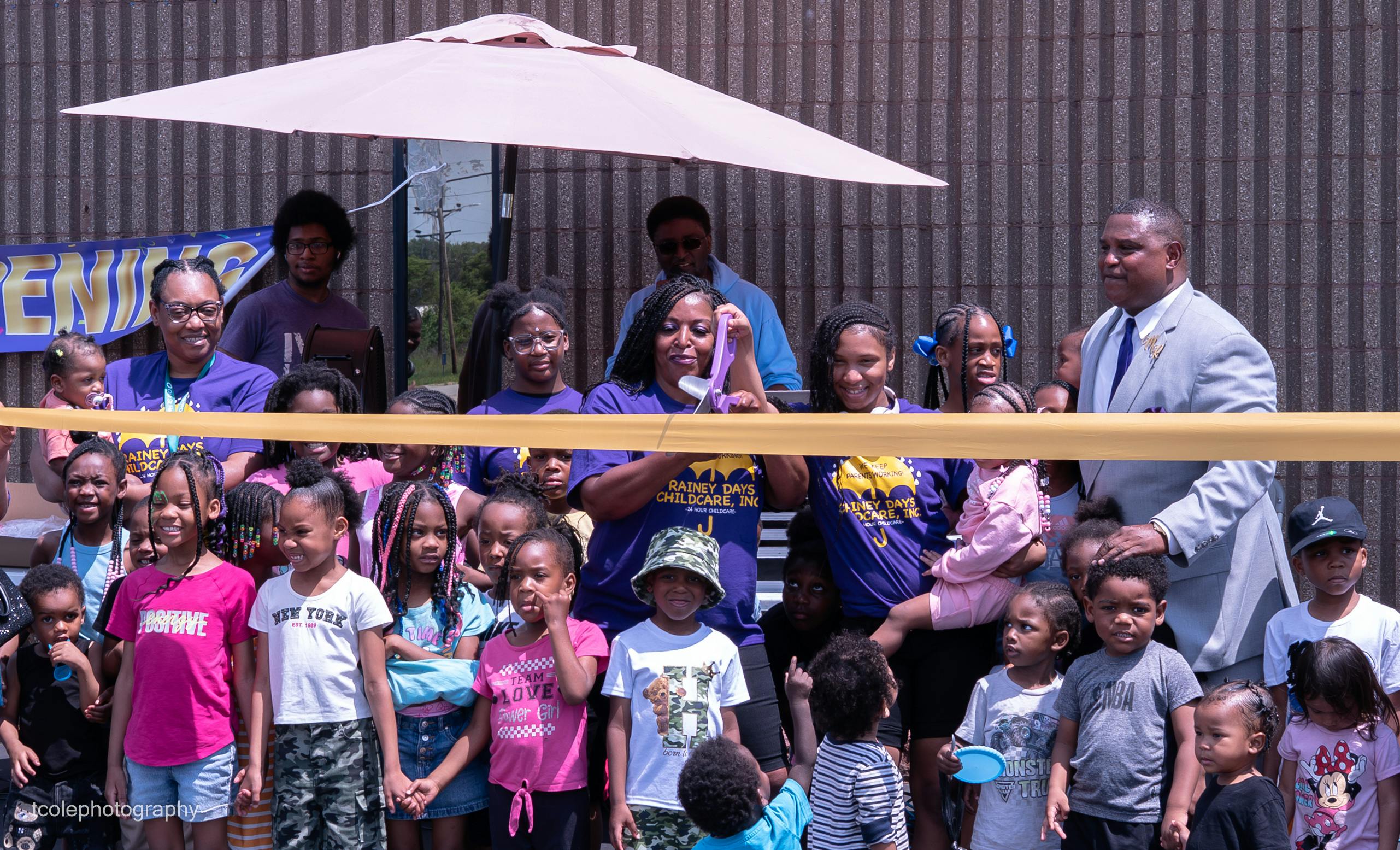 Adults and children gathered behind a yellow ribbon