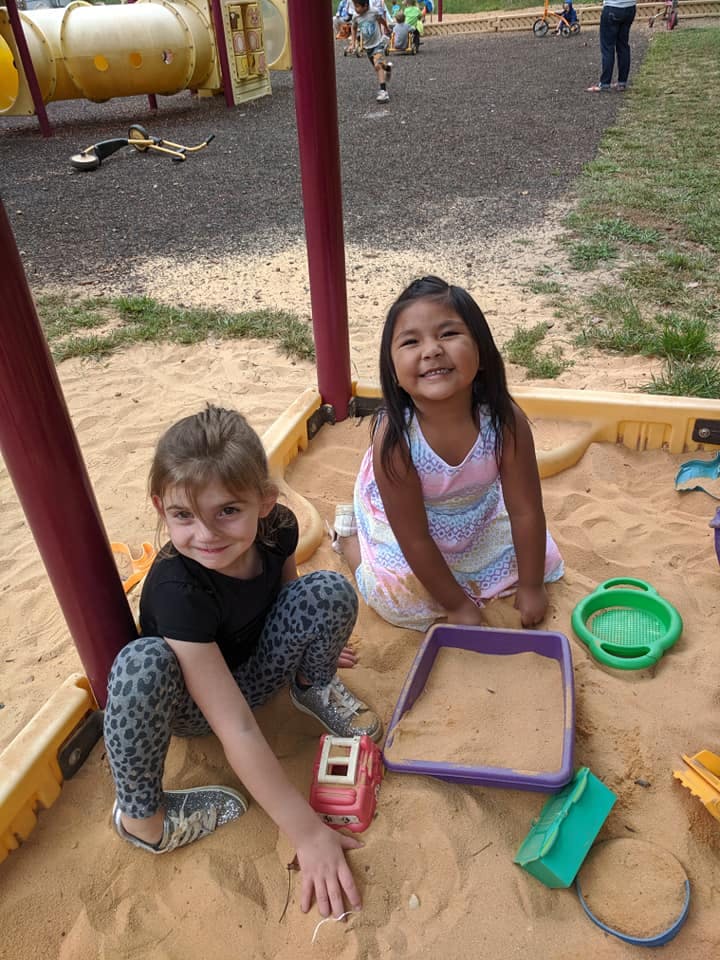 Two children playing in a sandbox with toys