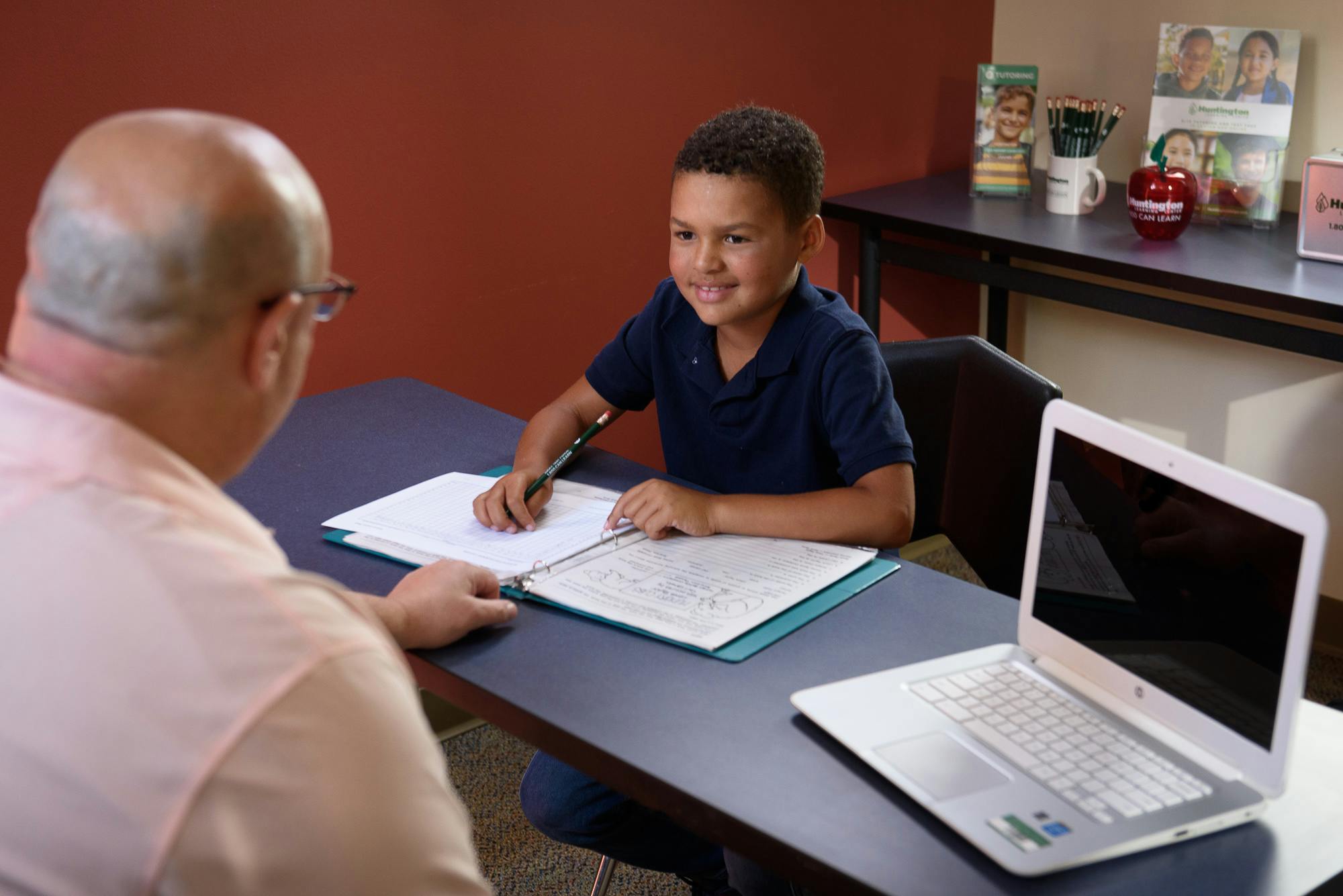 A person sitting across from a child writing in a binder at a desk