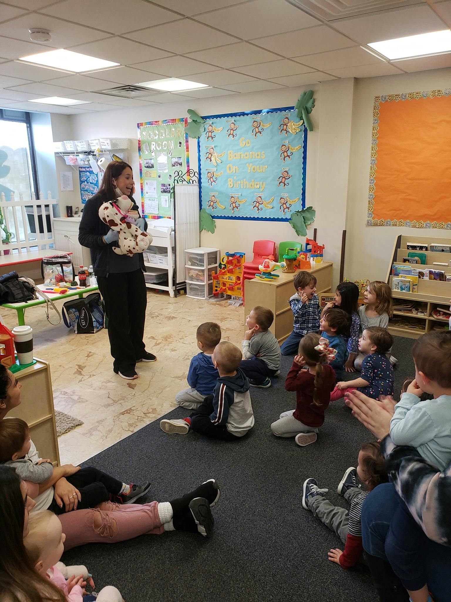 Person holding a stuffed animal in front of children in a classroom