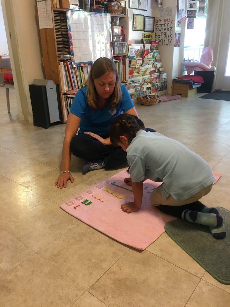Person and child kneeling on floor looking at a pink mat