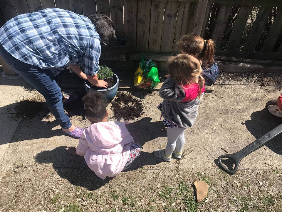 Person planting in a pot with two children watching