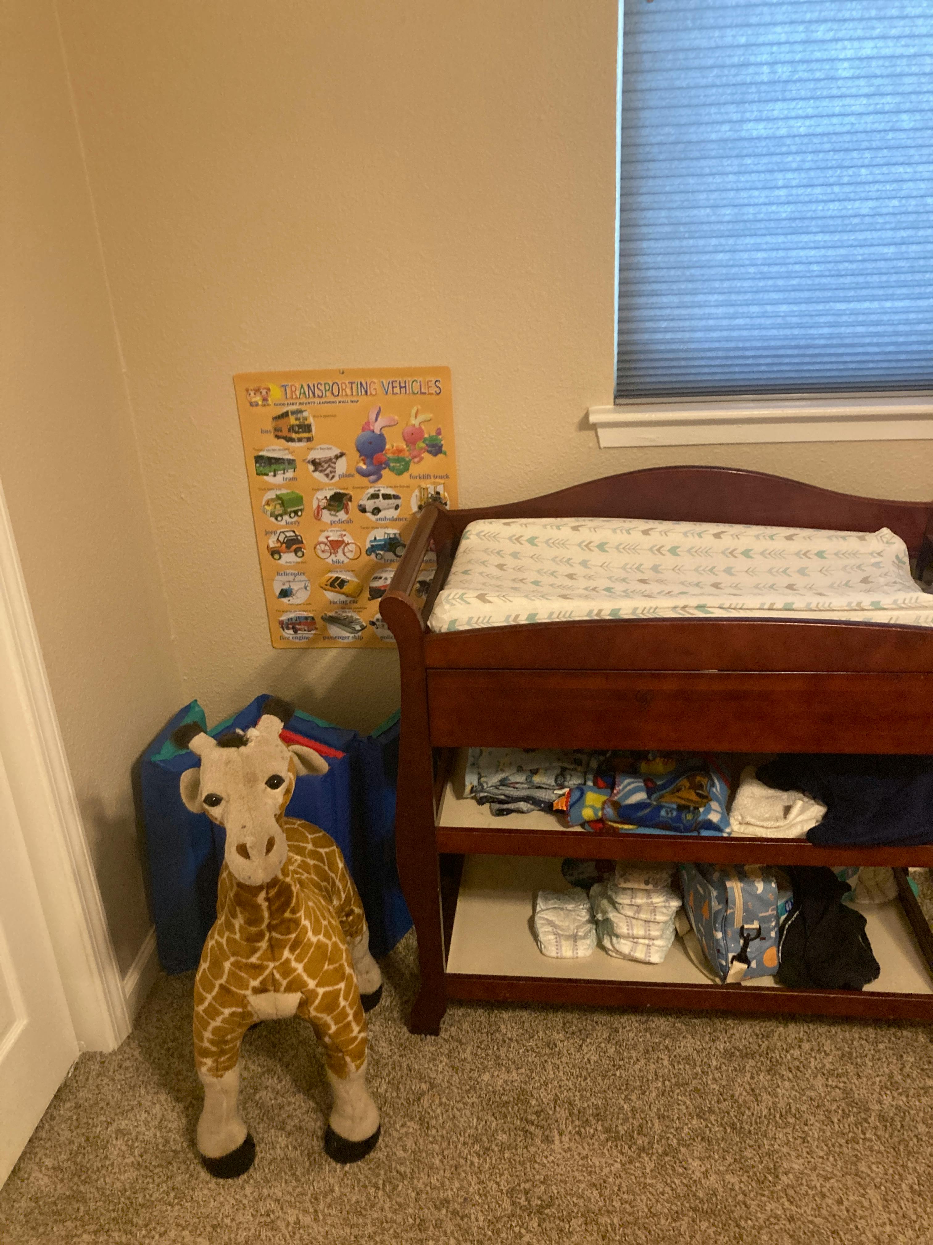 Stuffed giraffe toy next to a changing table with a poster on the wall