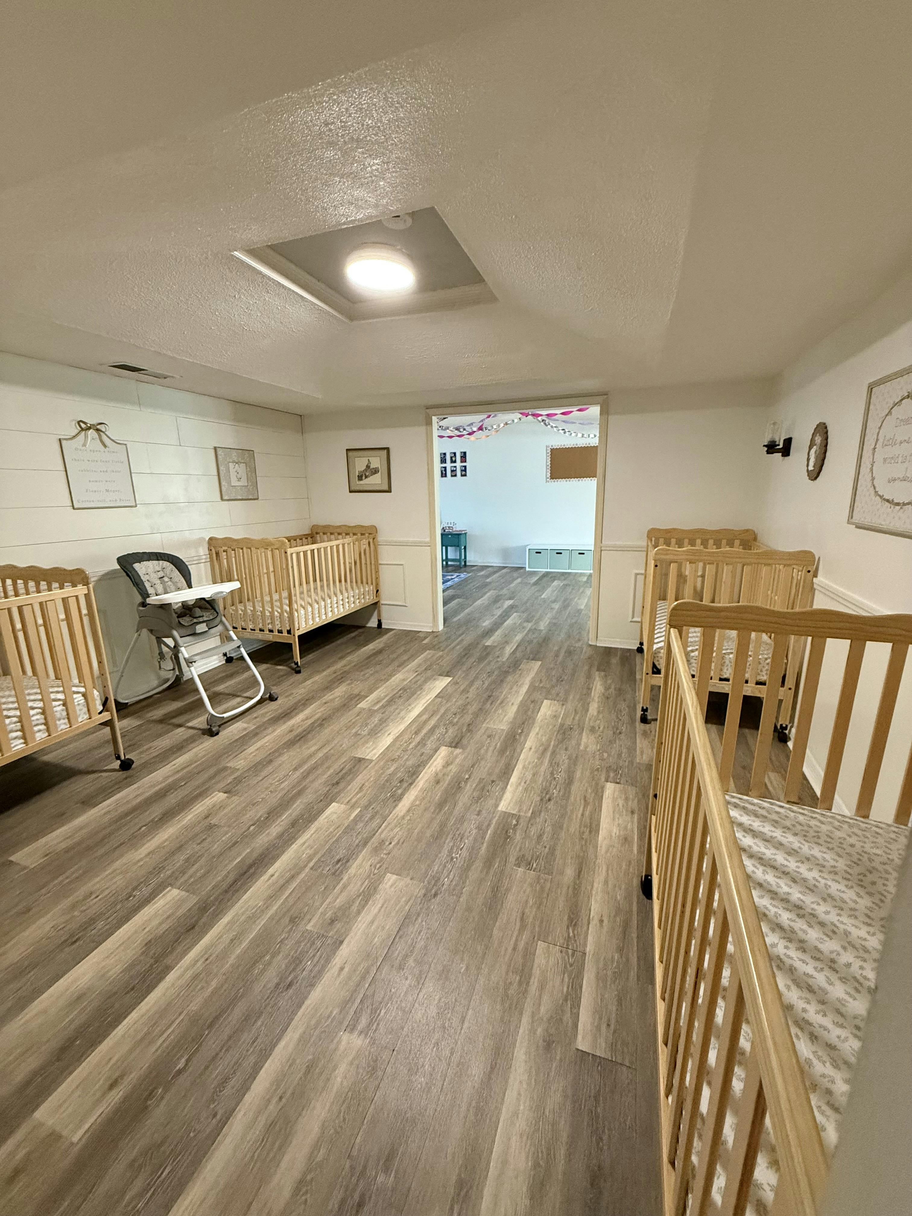 Multiple empty wooden cribs in a room with wood-like flooring