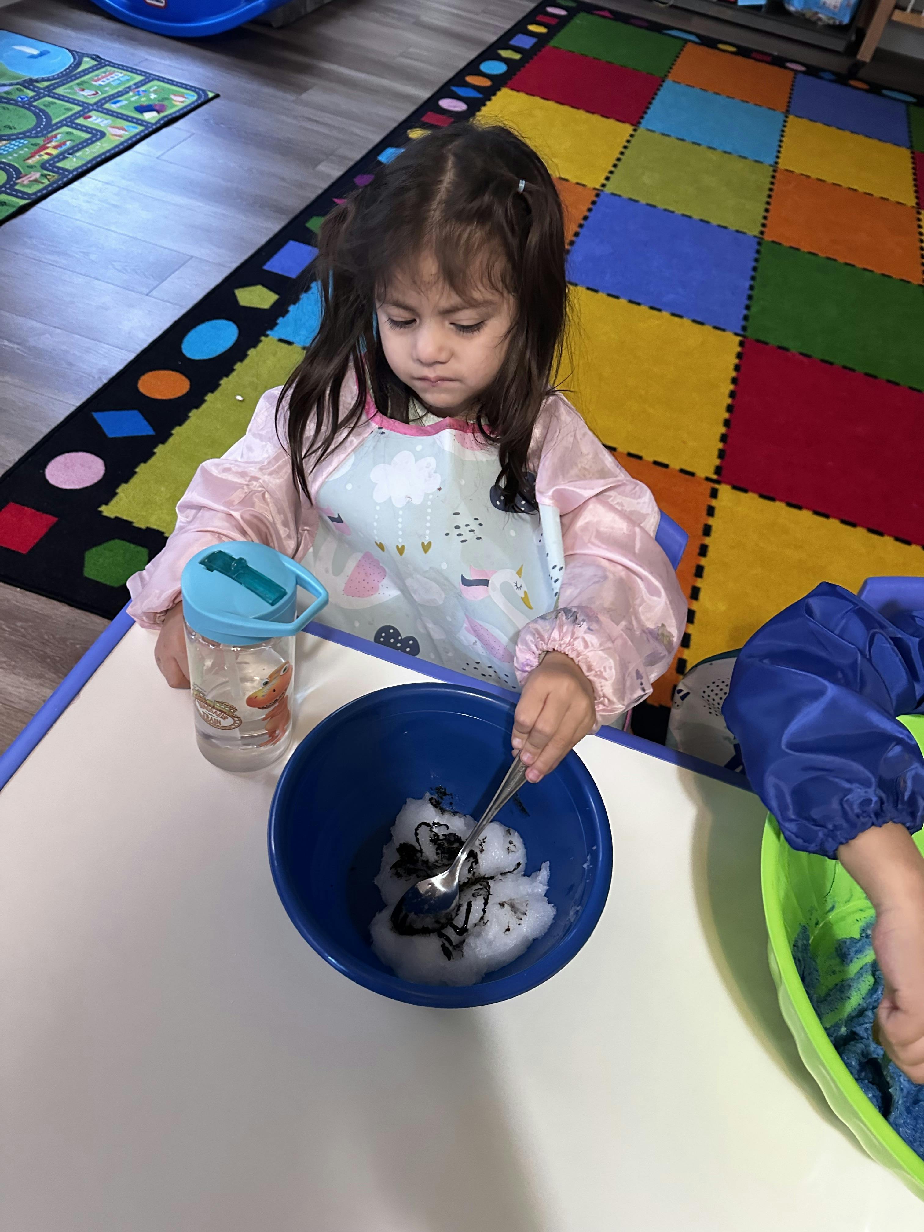 Child mixing a black substance into snow in a blue bowl