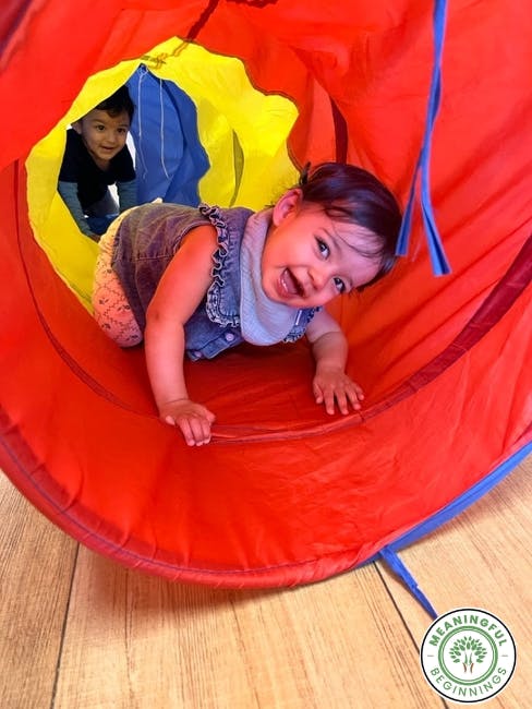 two children crawling through a colorful play tunnel