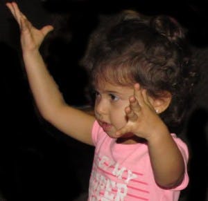 Child with one arm raised and the other hand near their face