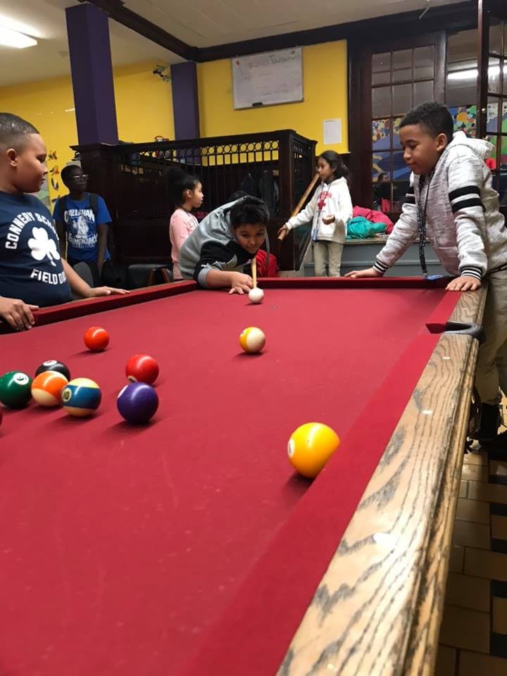 Child playing pool, aiming with a cue stick
