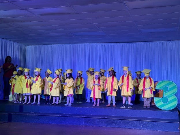 Group of children wearing yellow graduation caps and gowns on a stage