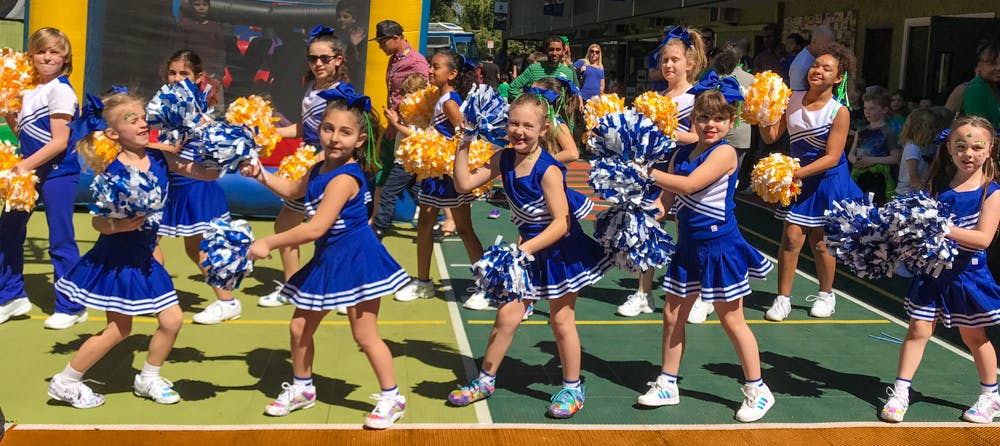 Children in blue and white cheerleading outfits holding pom-poms