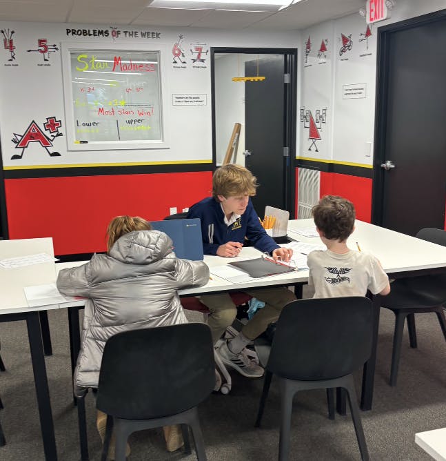 Three children working at a table in a classroom