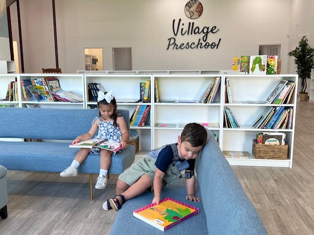 Two children reading books on blue couches in a room with bookshelves