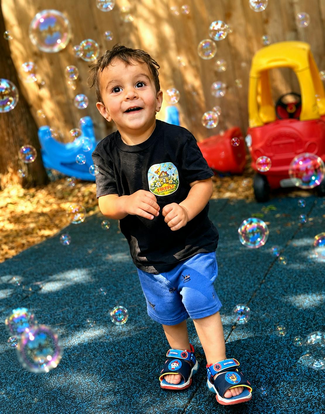 Child standing outdoors among bubbles