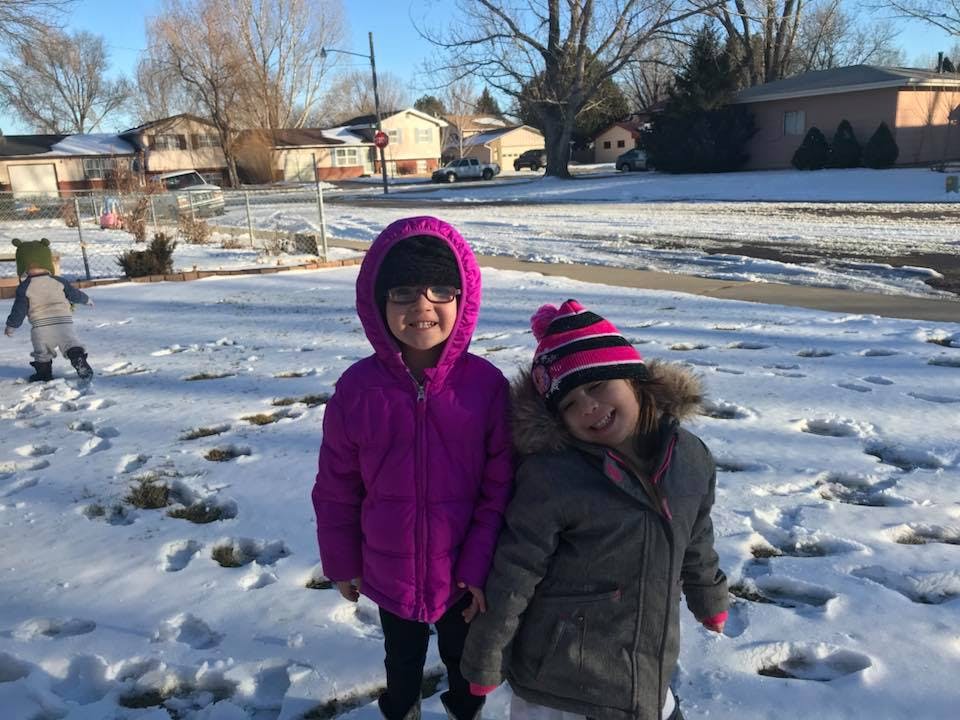 Two children standing in snow, another child in background