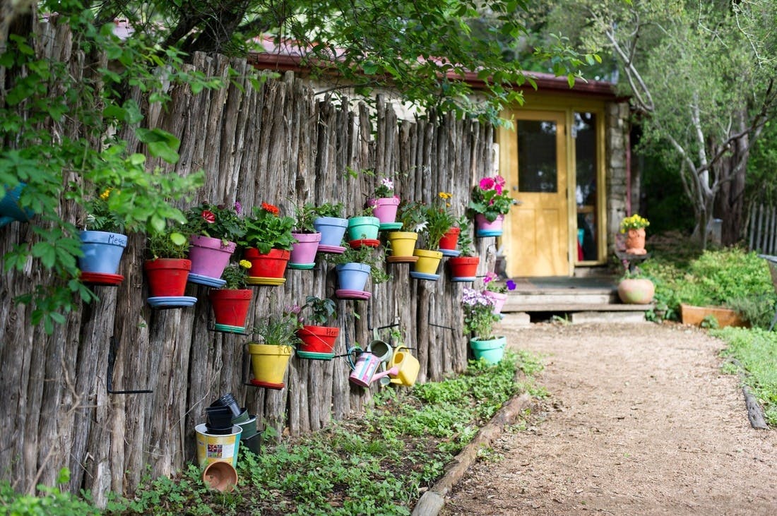 Wooden fence with colorful potted plants and a small building with a yellow door