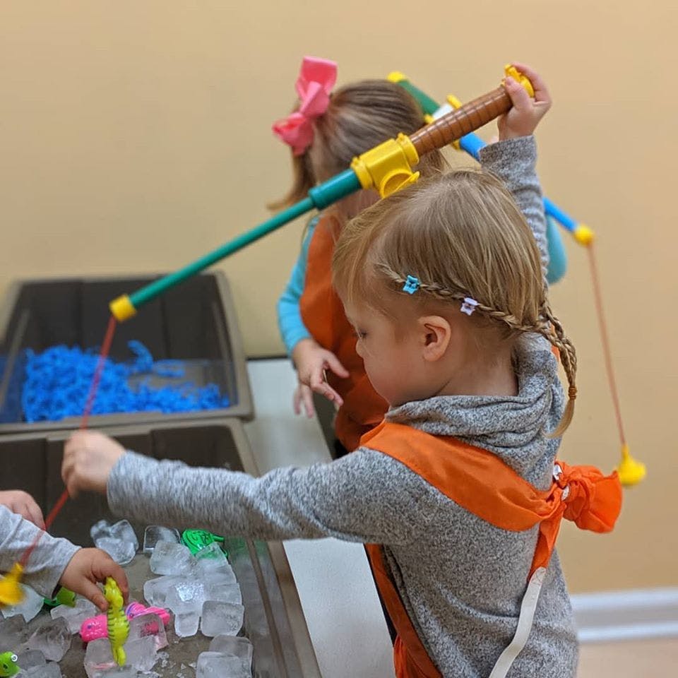 Child playing with a toy fishing rod, another child in the background