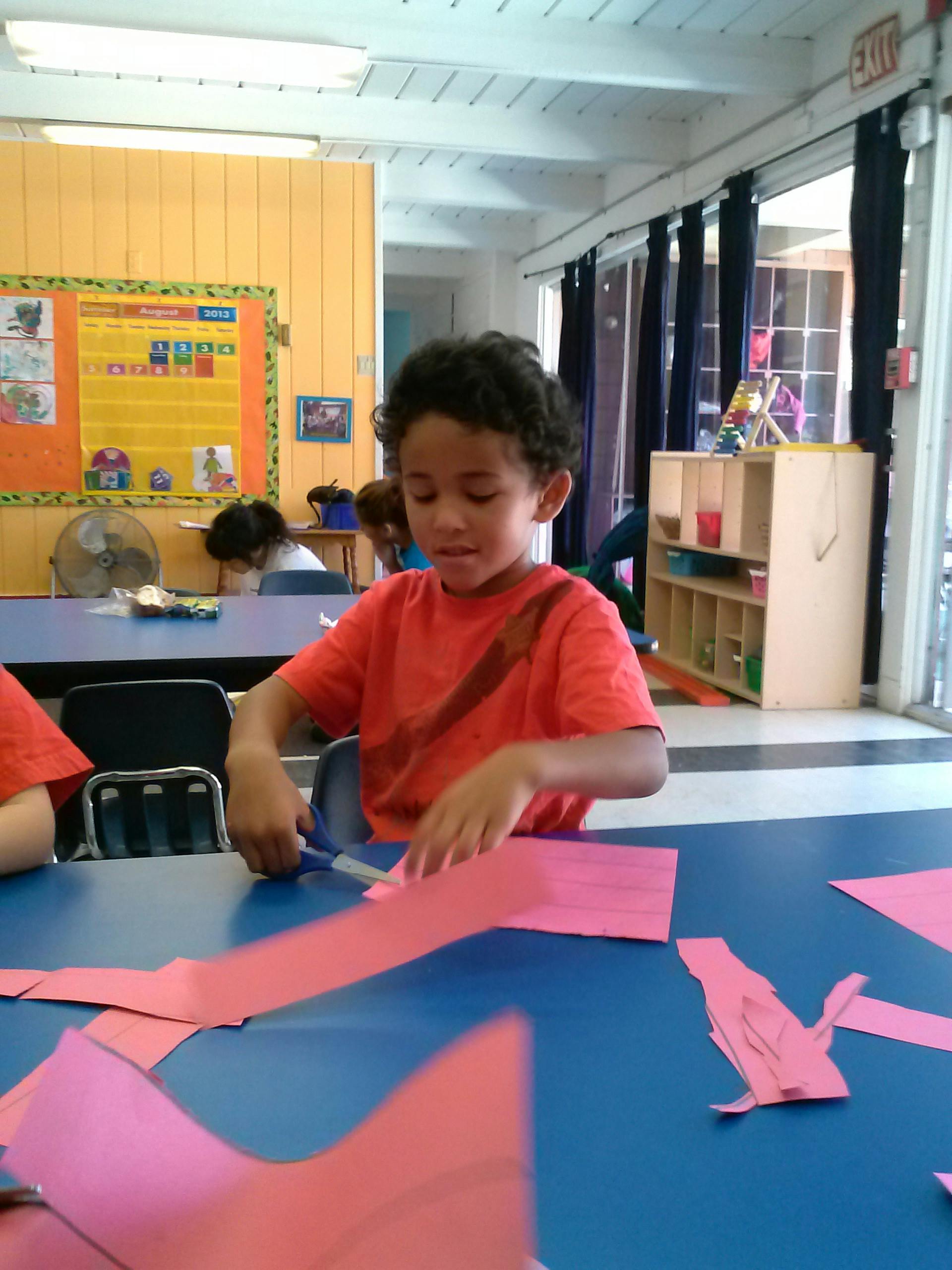 Child cutting pink paper with scissors in a classroom