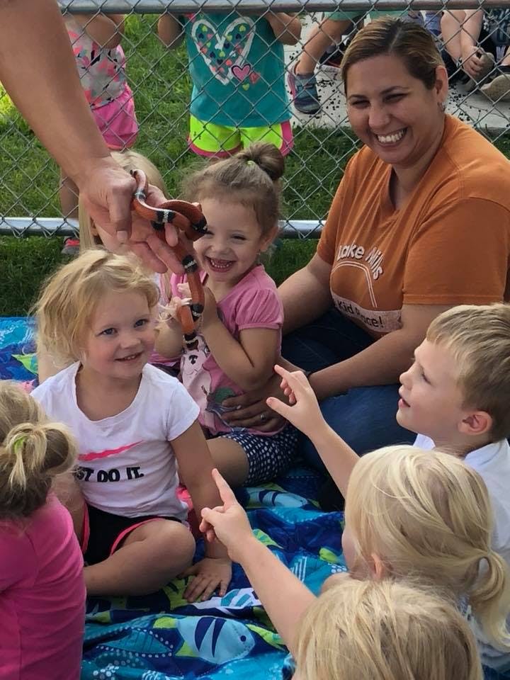 Person holding a toy snake for a child, with other children and an adult nearby