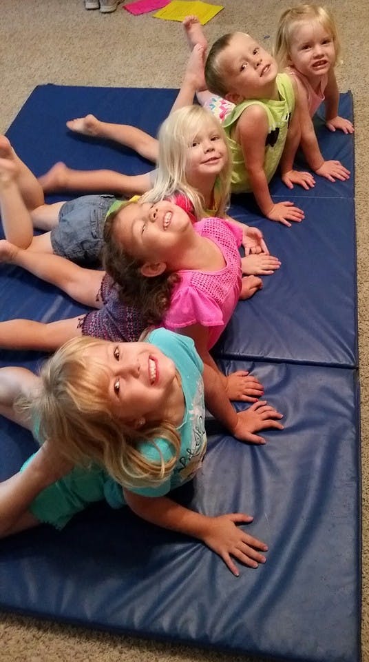 Five children lying on their stomachs on a blue mat