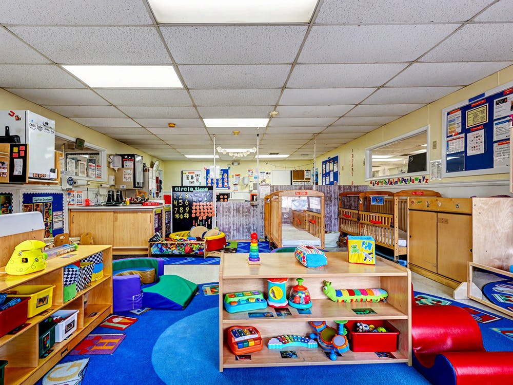 A colorful daycare room with play mats, toys, and cribs